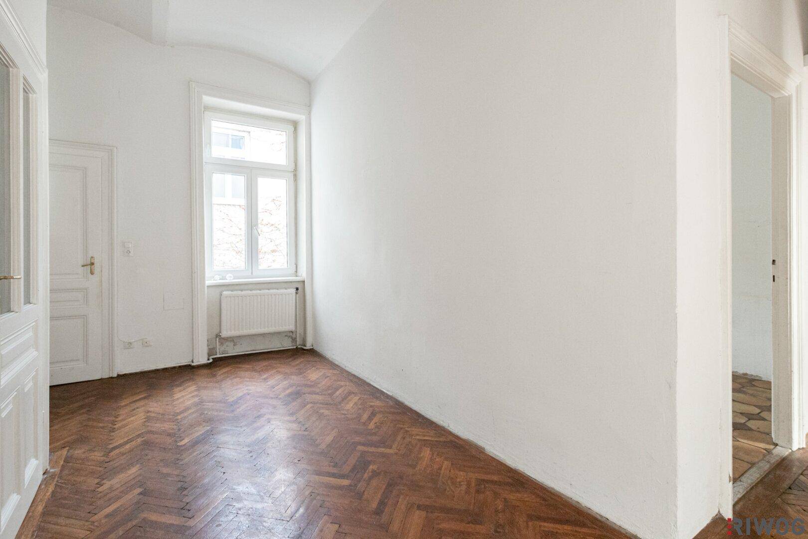 Leeres Zimmer mit Fischgrätparkett und hohen Fenstern, ideal als Schlaf- oder Arbeitszimmer.