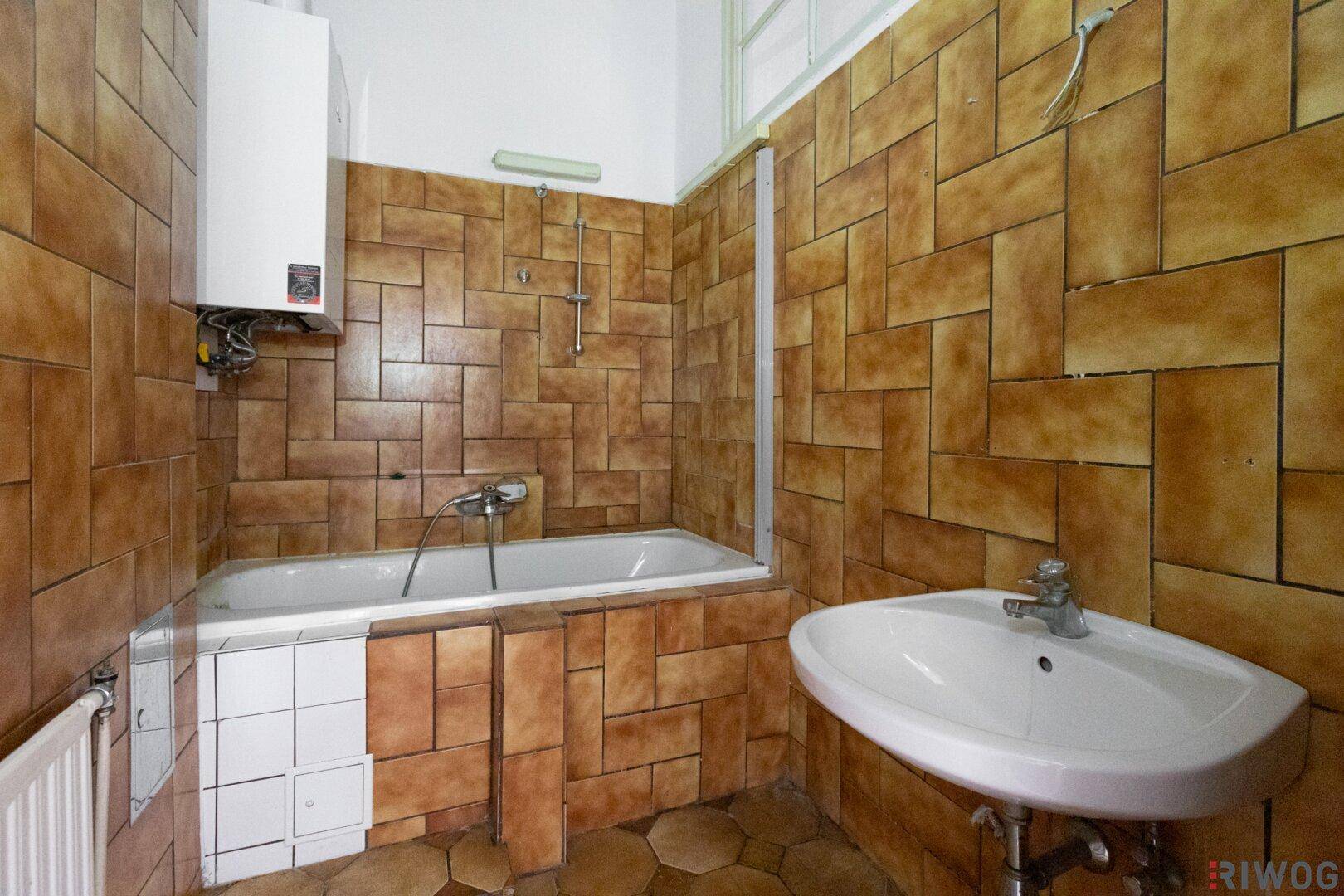 Badezimmer mit braunen Fliesen, Badewanne und Waschbecken, ausgestattet mit Gastherme.