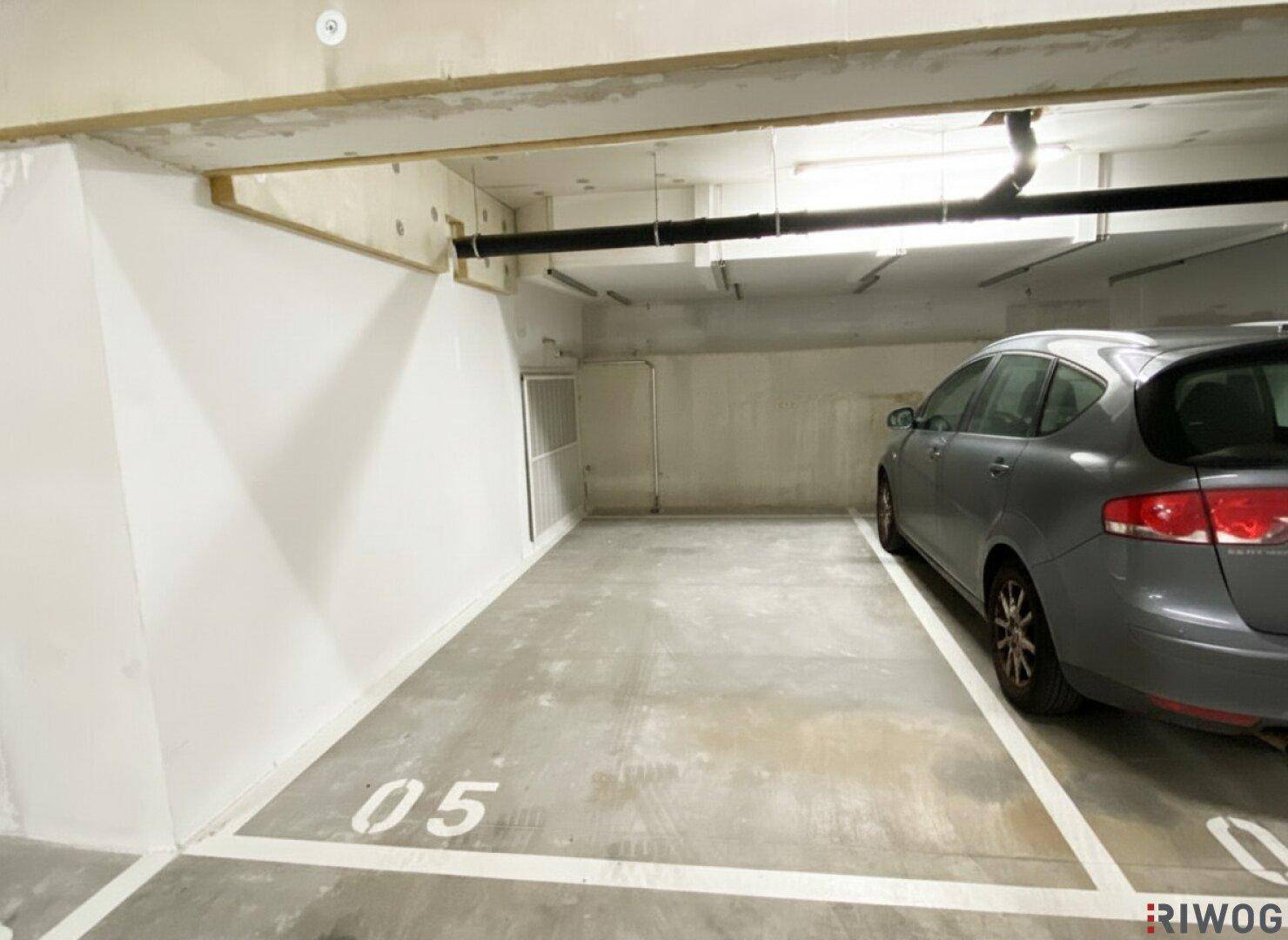 Tiefgaragenstellplatz mit einem grauen Auto und einer weißen Wand im Hintergrund, gut beleuchtet.