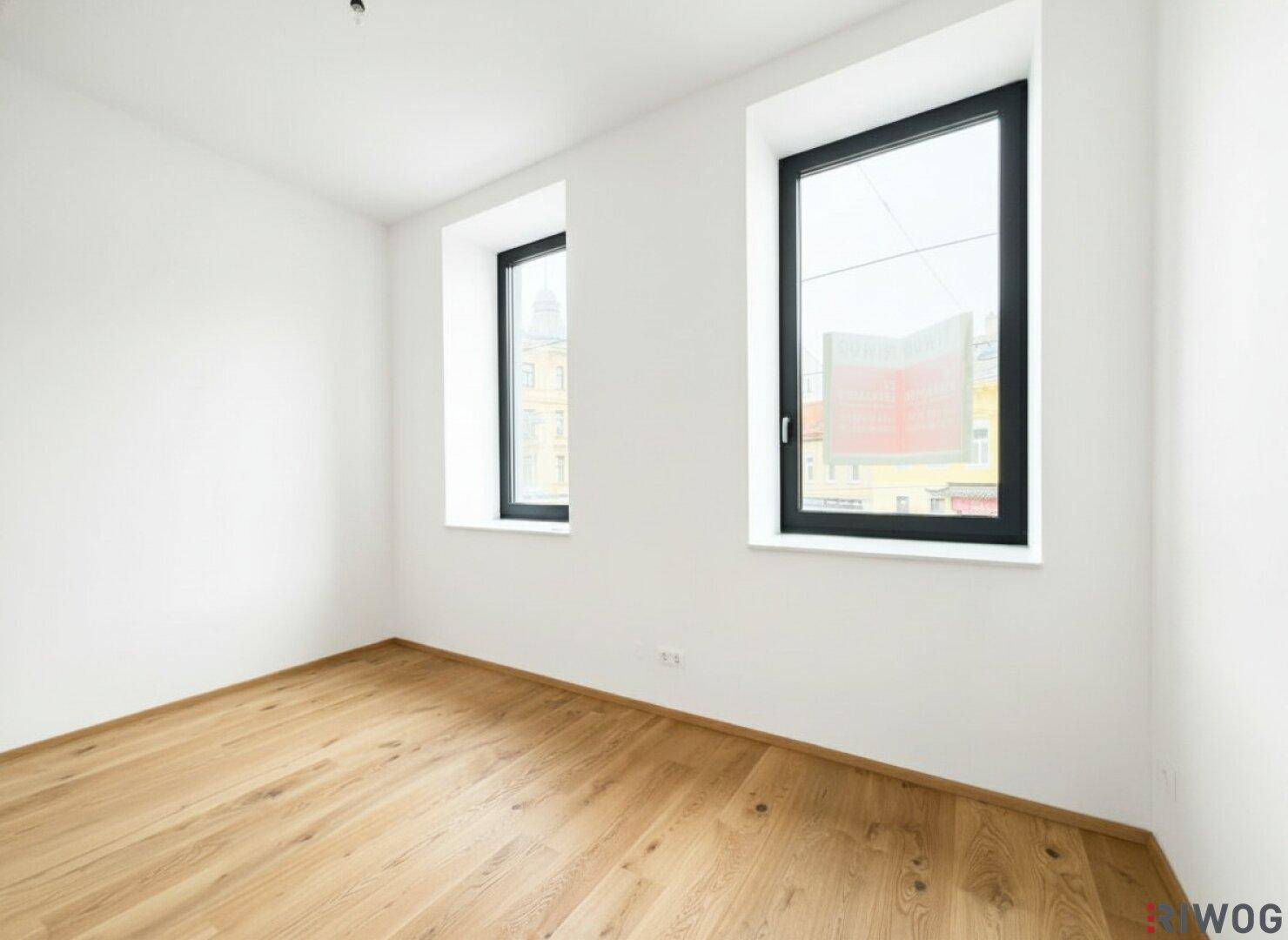 Lichtdurchfluteter Raum mit elegantem Holzparkett und zwei hohen Fenstern, die einen weiten Stadtblick ermöglichen.
