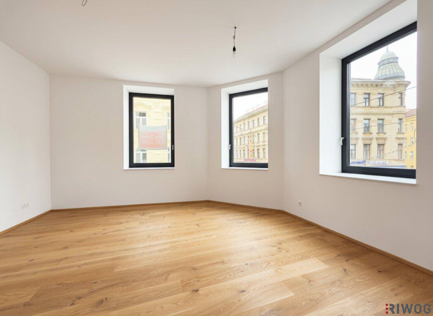 Geräumiges Zimmer mit geschwungener Wand, hochwertigem Holzparkett und mehreren Fenstern mit Stadtblick.