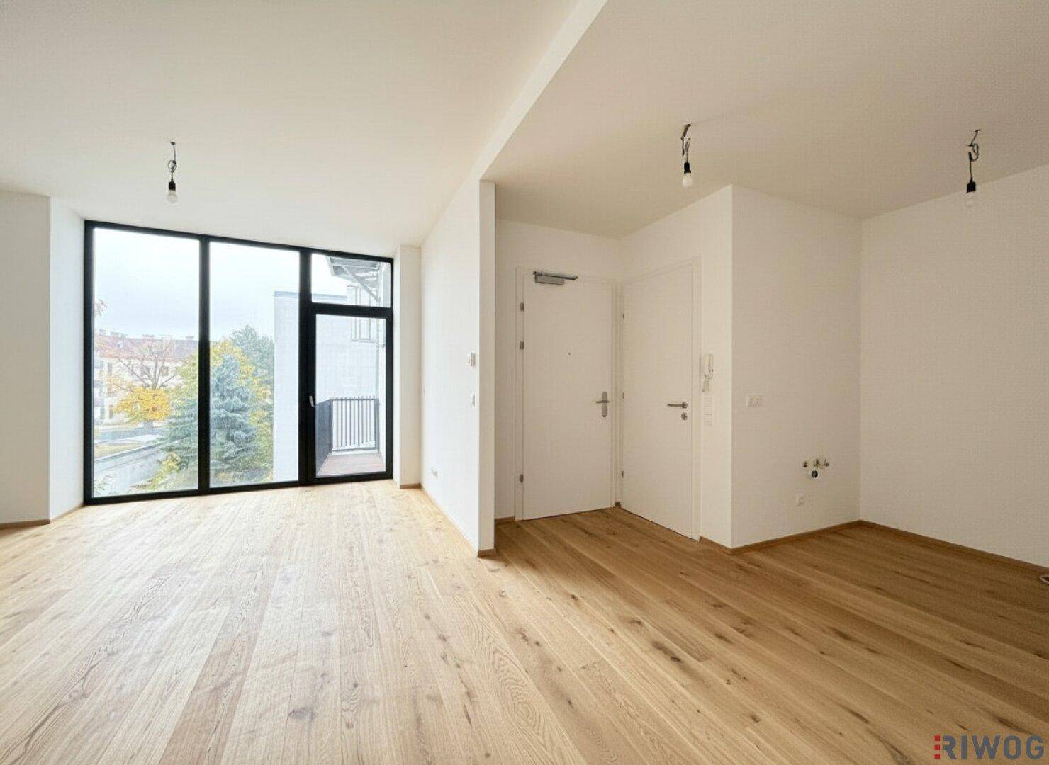 Heller Wohnbereich mit großflächigen Fenstern, Holzparkett und direktem Zugang zu einem Balkon oder einer Terrasse.
