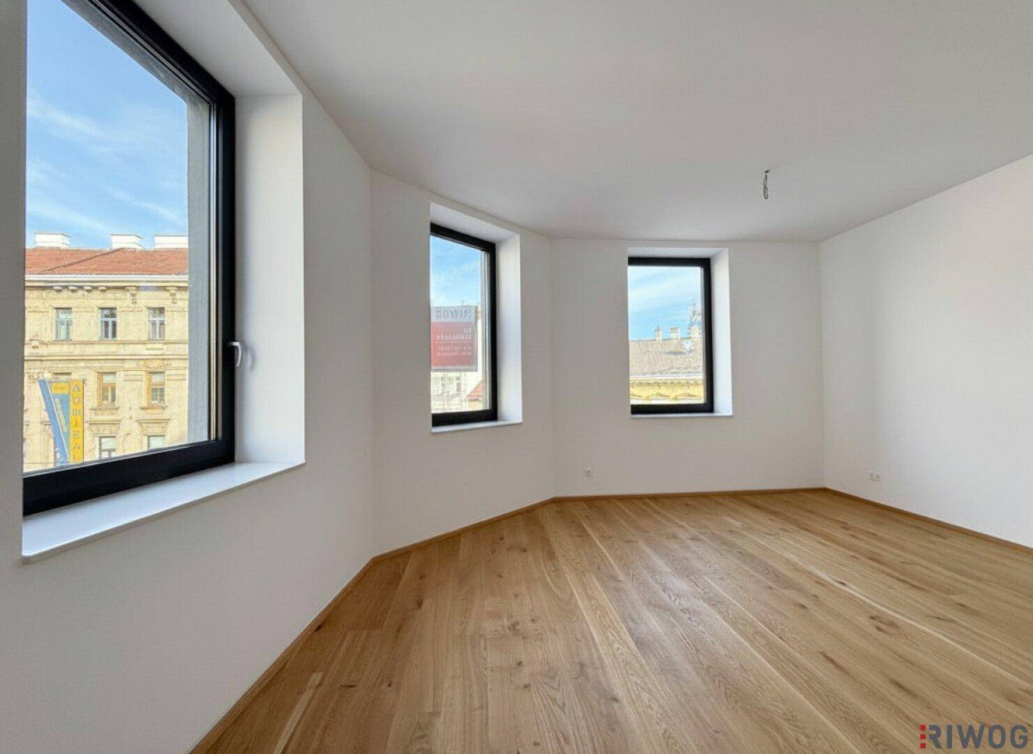 Heller Raum mit Holzparkett, weiß gestrichenen Wänden und mehreren Fenstern, die einen weiten Blick auf die Umgebung bieten.