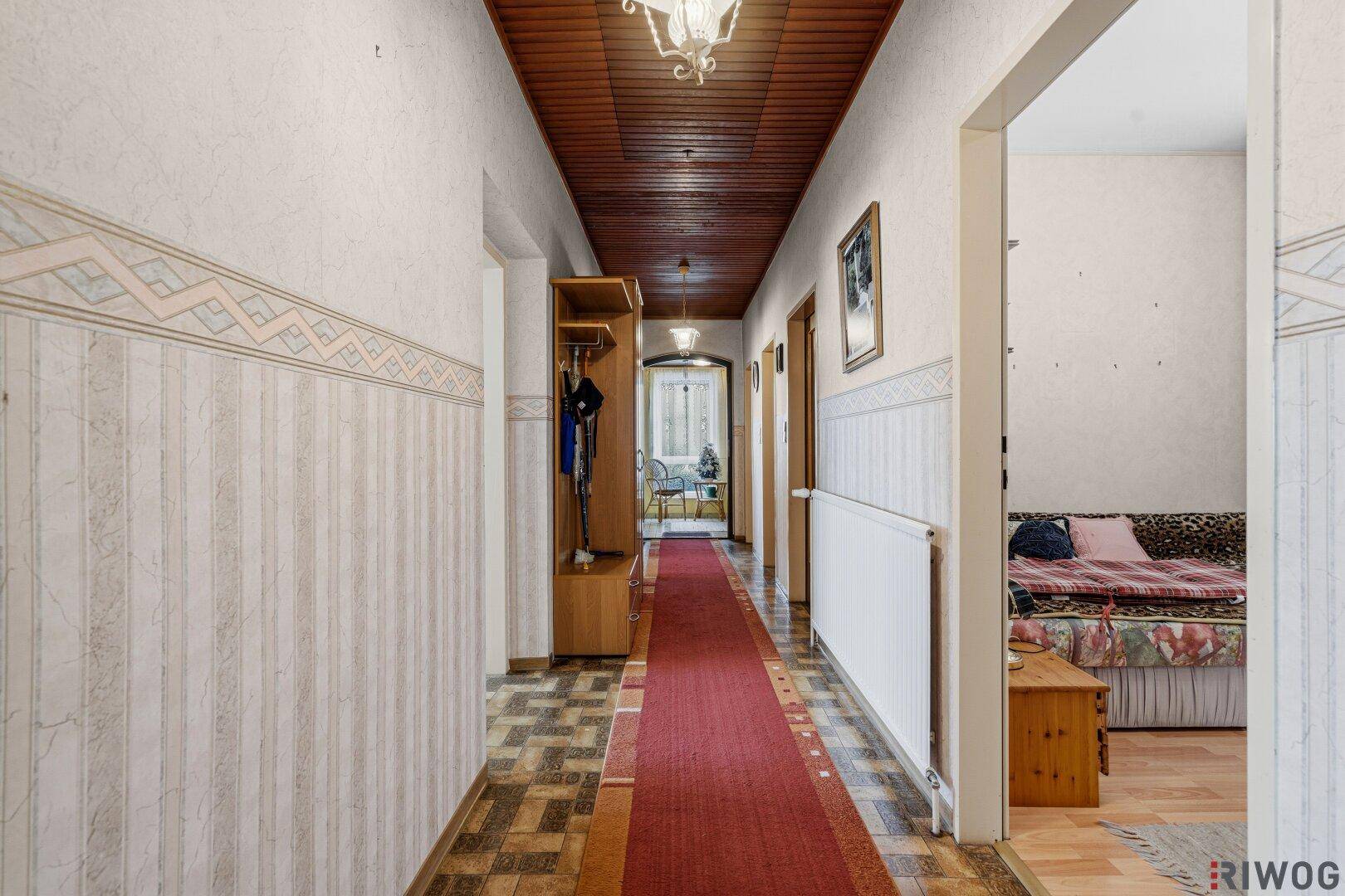 Weiterer Blick in den Flur mit Holzdecke, Heizkörper und Zugang zu einem angrenzenden Schlafzimmer.