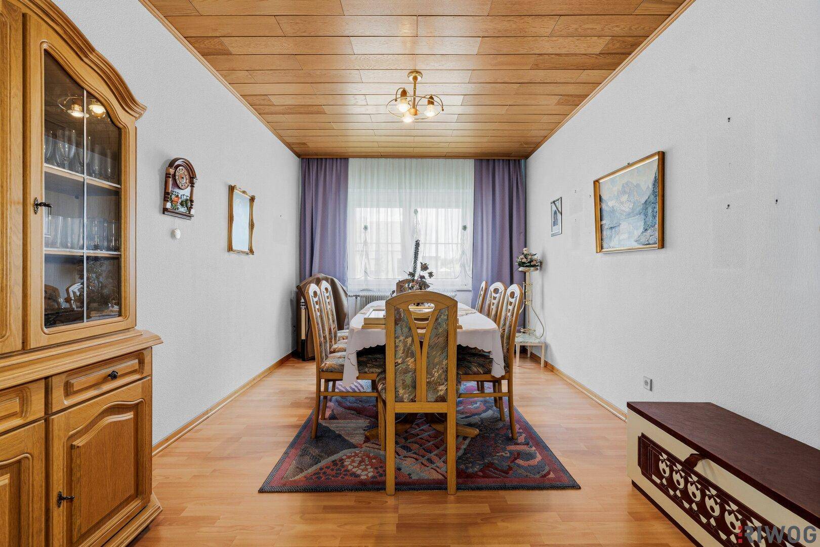 Geräumiges Esszimmer mit großem Holztisch, passenden Stühlen, Vitrine und einer Holzdecke.
