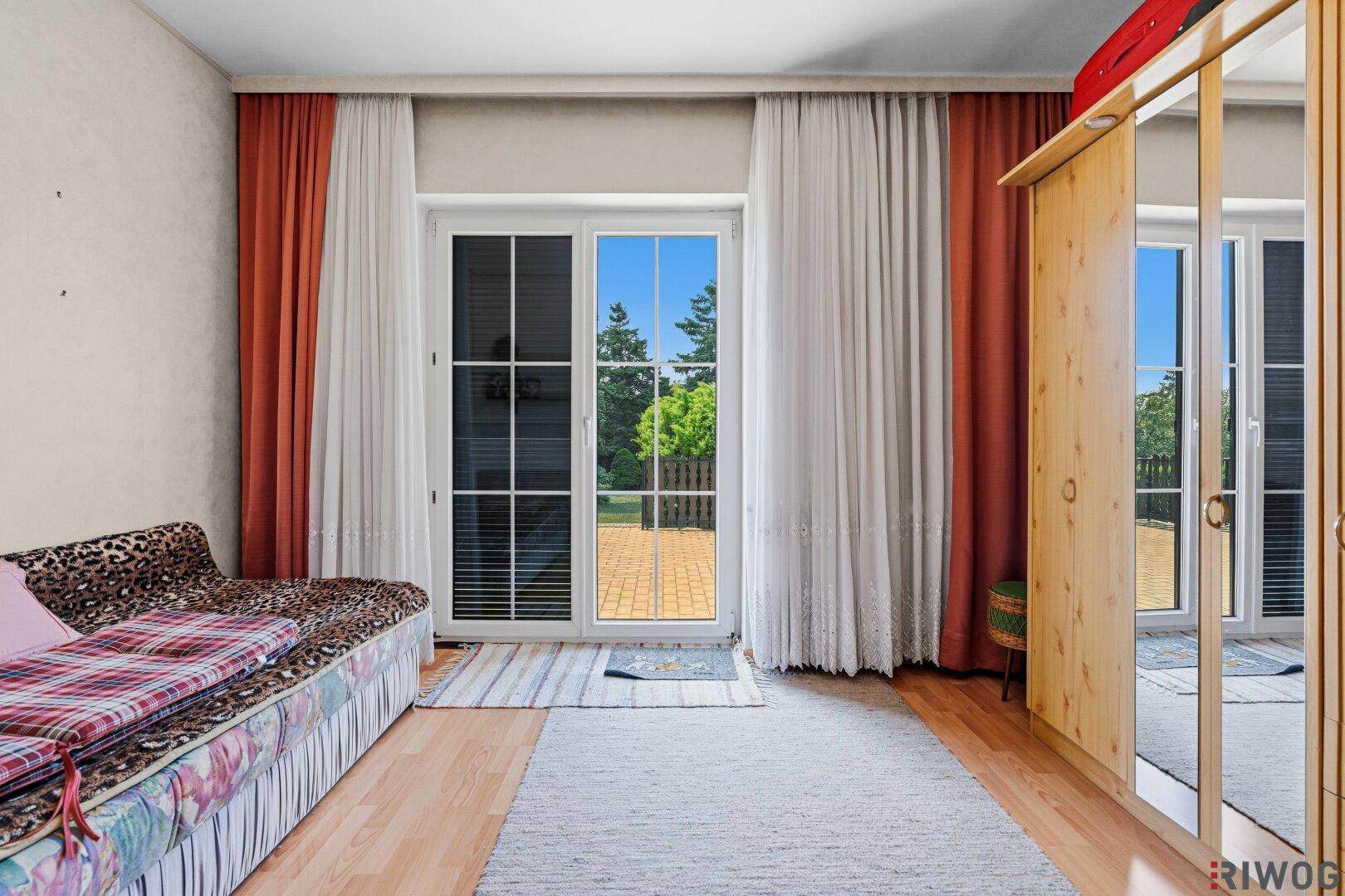 Schlafzimmer mit Tagesbett, Holzschrank und großer Fenstertür, die ins Freie führt.