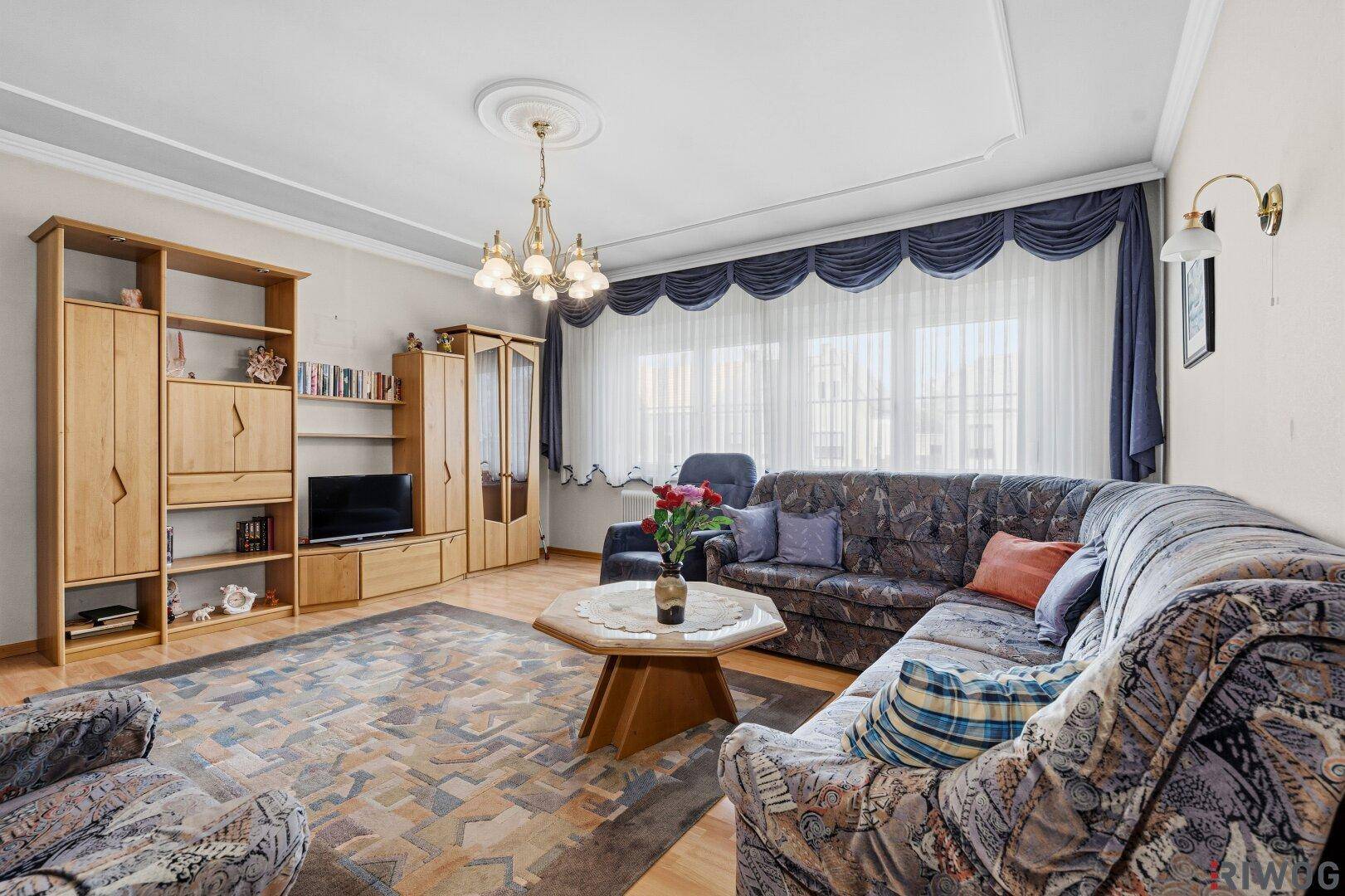 Geräumiges Wohnzimmer mit großem Sofa, Sesseln, Holzmöbeln und einer dekorativen Deckenrosette.