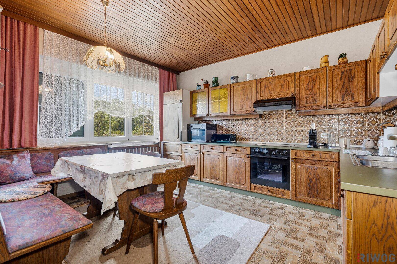 Traditionelle Küche mit Holzschränken, gemusterten Fliesen, Essecke und einer Holzdecke.