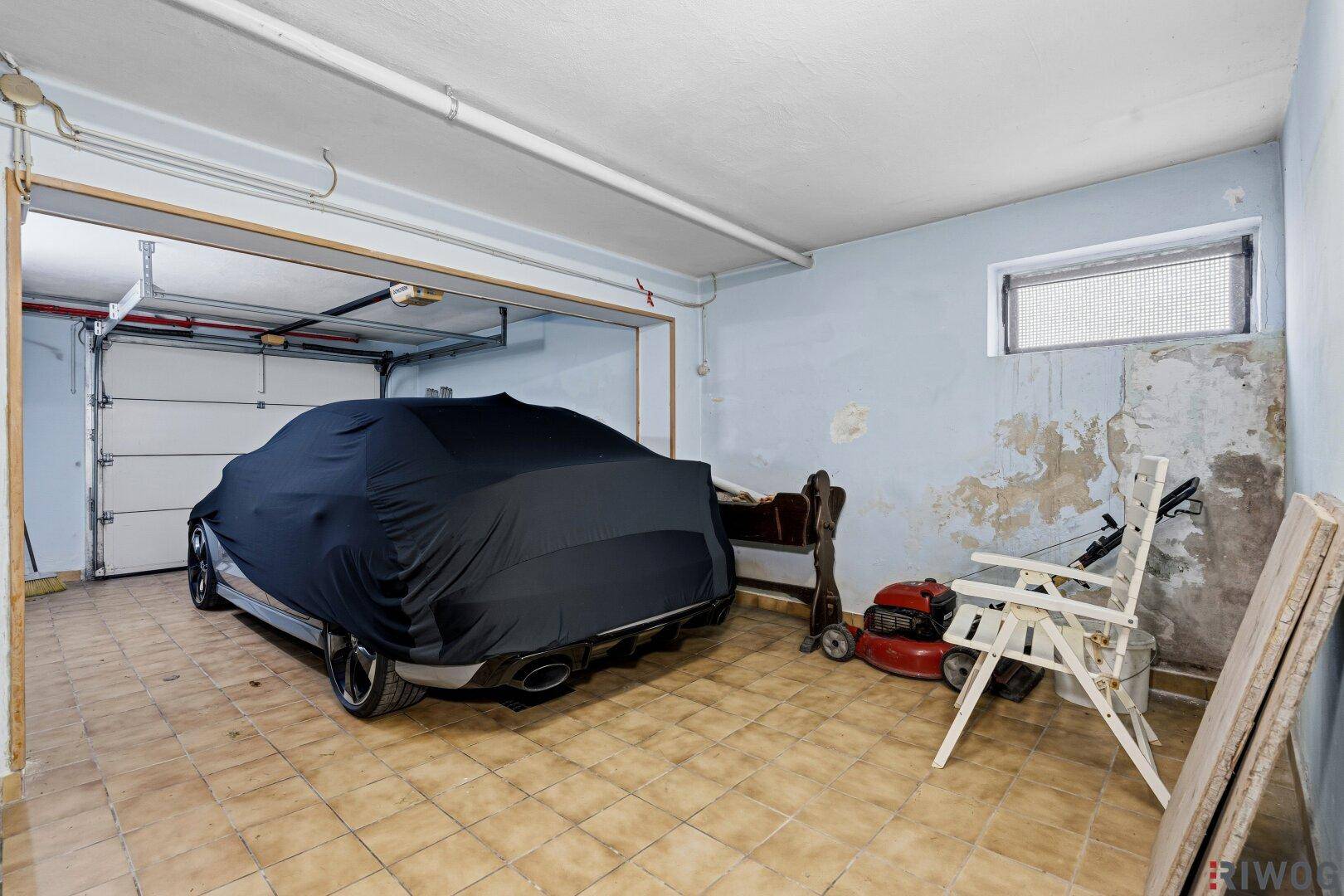 Garage mit einem abgedeckten Auto, Fliesenboden und verschiedenen Lagergegenständen.