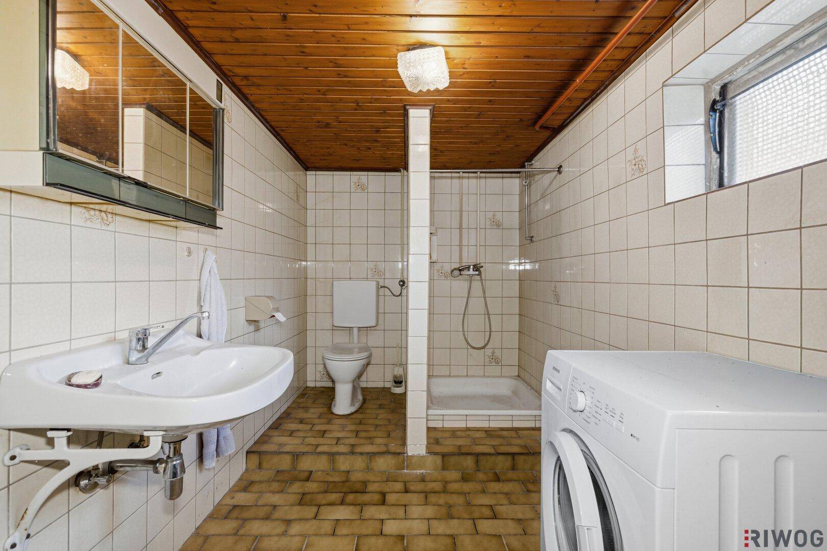 Kellerbad/Hauswirtschaftsraum mit Dusche, Toilette, Waschbecken und Waschmaschine.