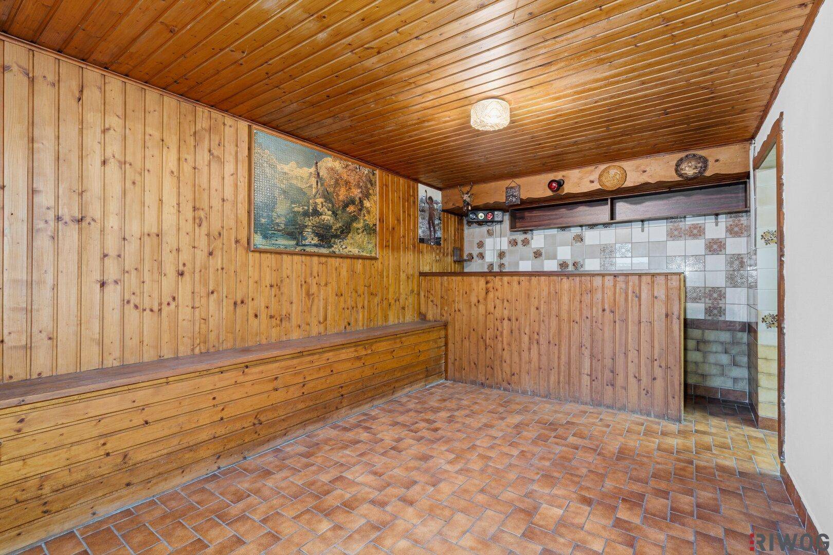 Kellerraum mit holzvertäfelten Wänden und Decke, Fliesenboden und einer eingebauten Sitzbank.