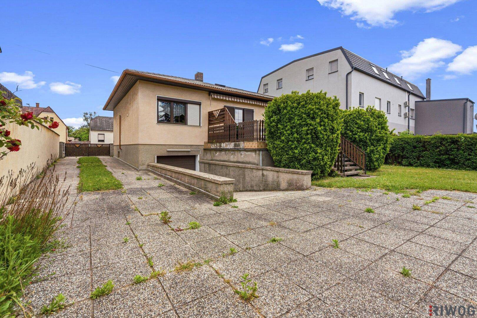 Außenansicht des Hauses mit großer gepflasterter Fläche, Auffahrt und Zugang zur Kellergarage.