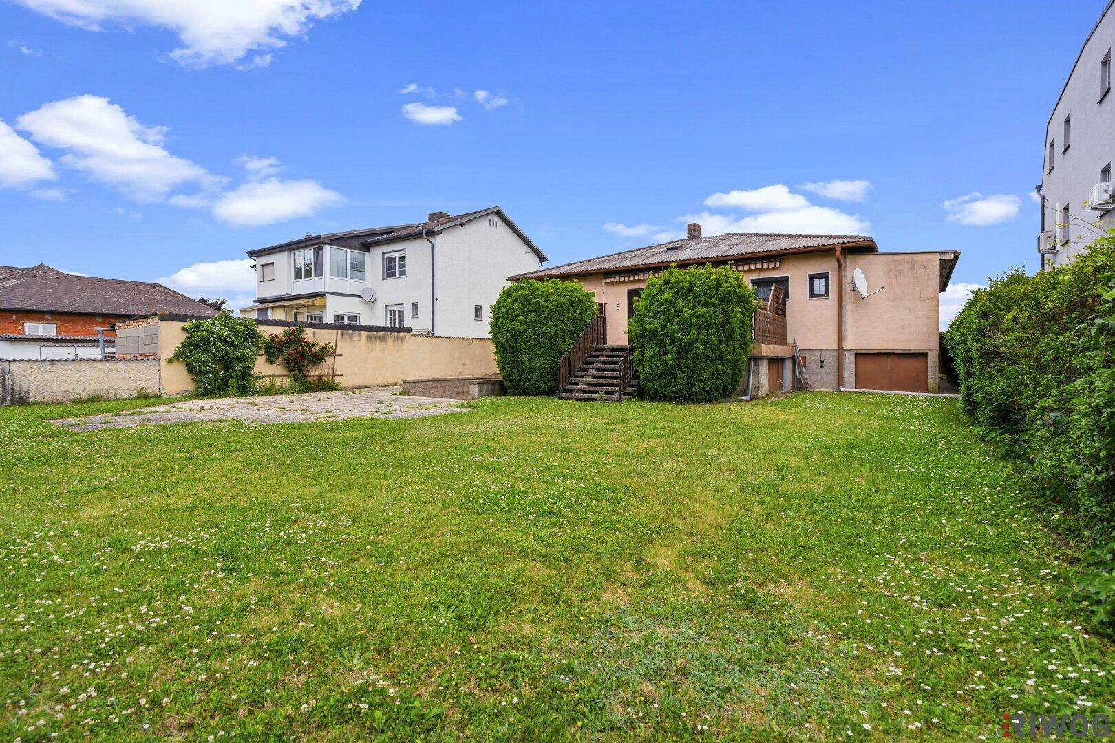 Großer Garten mit Rasenfläche und Blick auf die Rückseite des Einfamilienhauses mit Außentreppe.
