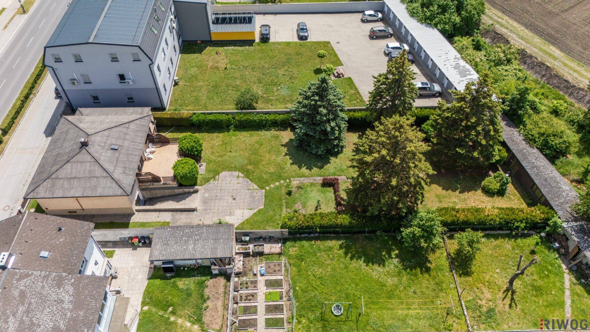 Luftaufnahme des Grundstücks mit Einfamilienhaus, Garten, Parkplätzen und angrenzenden Feldern.