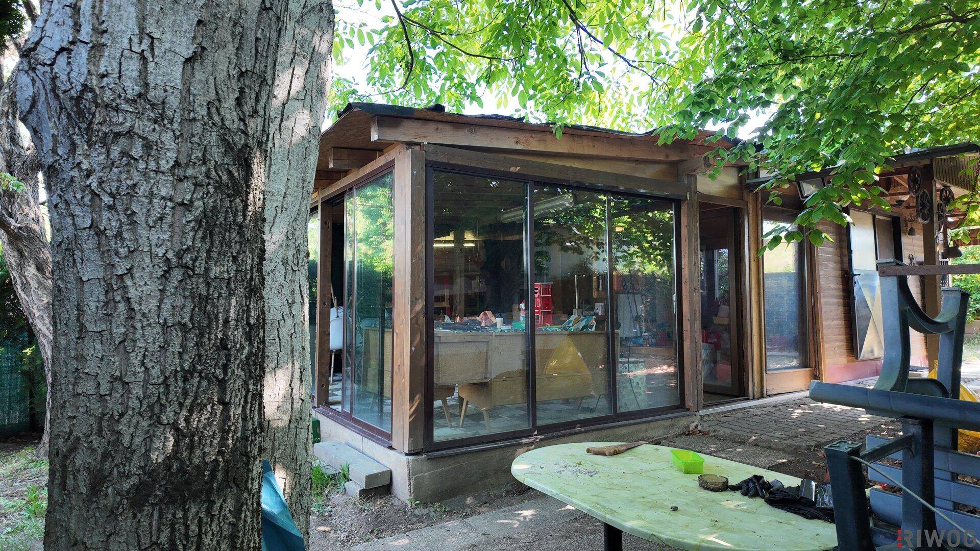 Außenseite des Gebäudes mit großen Glasfenstern und Holzelementen, umgeben von Bäumen.