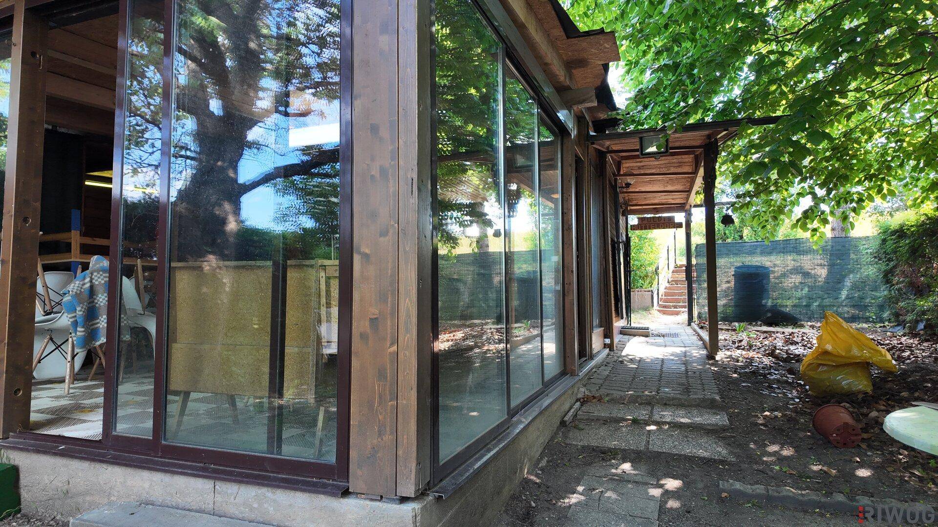 Außenseite des Gebäudes mit großen Glasfenstern und Holzelementen, umgeben von Bäumen und Grün.