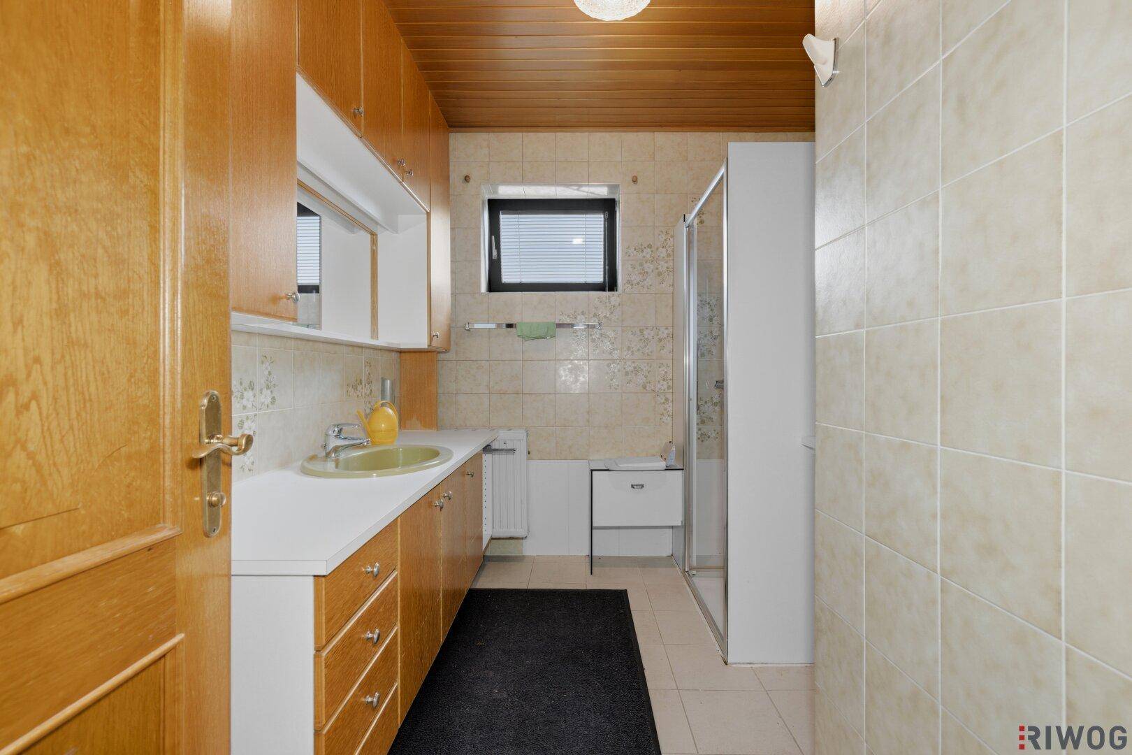 Badezimmer mit Holzdecke, beigen Fliesen, Einzelwaschbecken und Duschkabine.