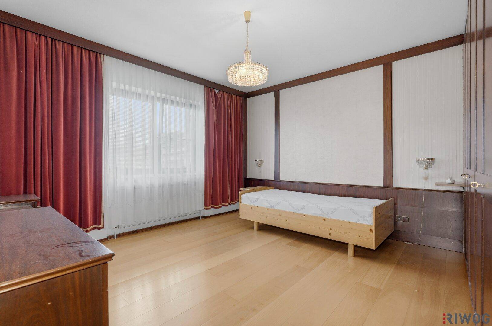 Schlafzimmer mit hellem Holzboden, großen Fenstern und einem einfachen Holzbett.