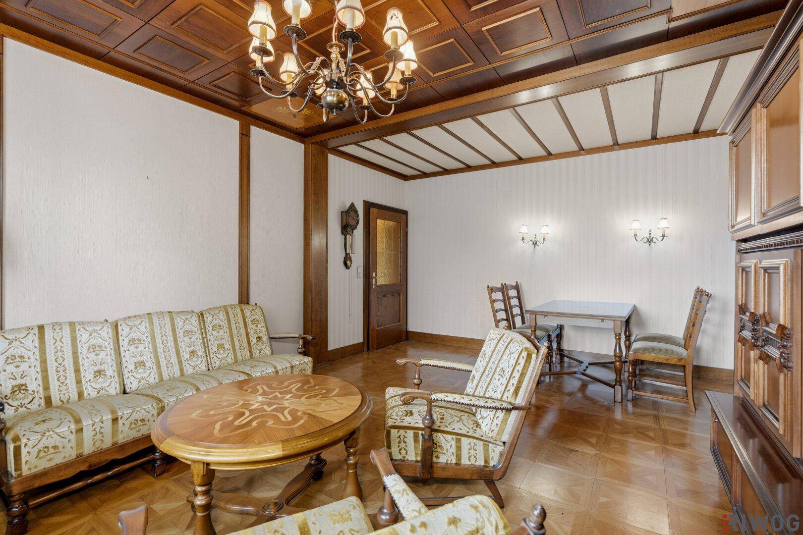 Gemütliches Wohnzimmer mit Holzkassettendecke, Parkettboden und traditionellen Sitzmöbeln.