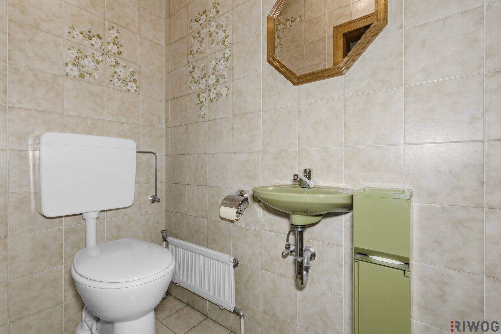 Gäste-WC mit beigen Fliesen, grünem Waschbecken und Toilette in traditionellem Stil.
