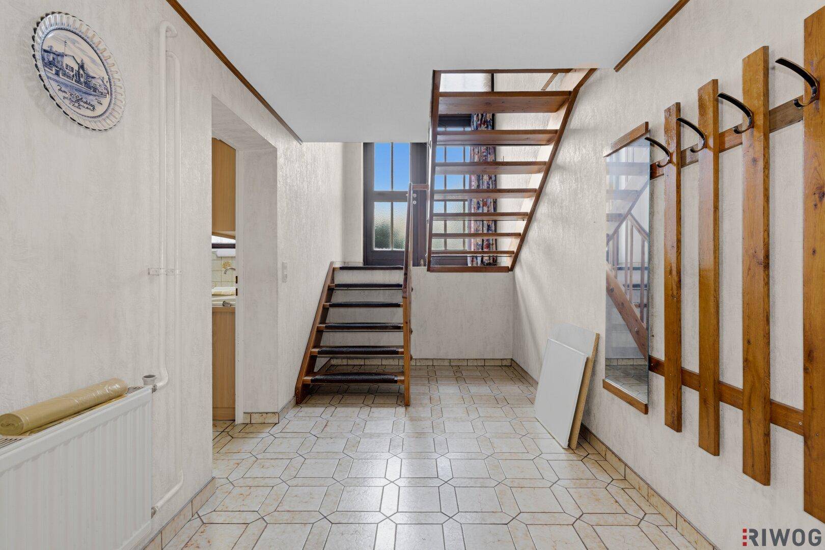 Eingangsbereich mit gefliestem Boden, Holztreppe und Garderobe.