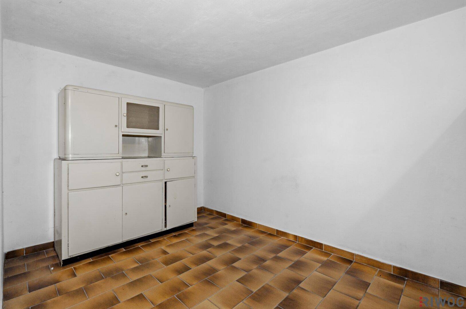 Kellerraum mit gefliestem Boden und einem alten Schrank, ideal als Abstellfläche.