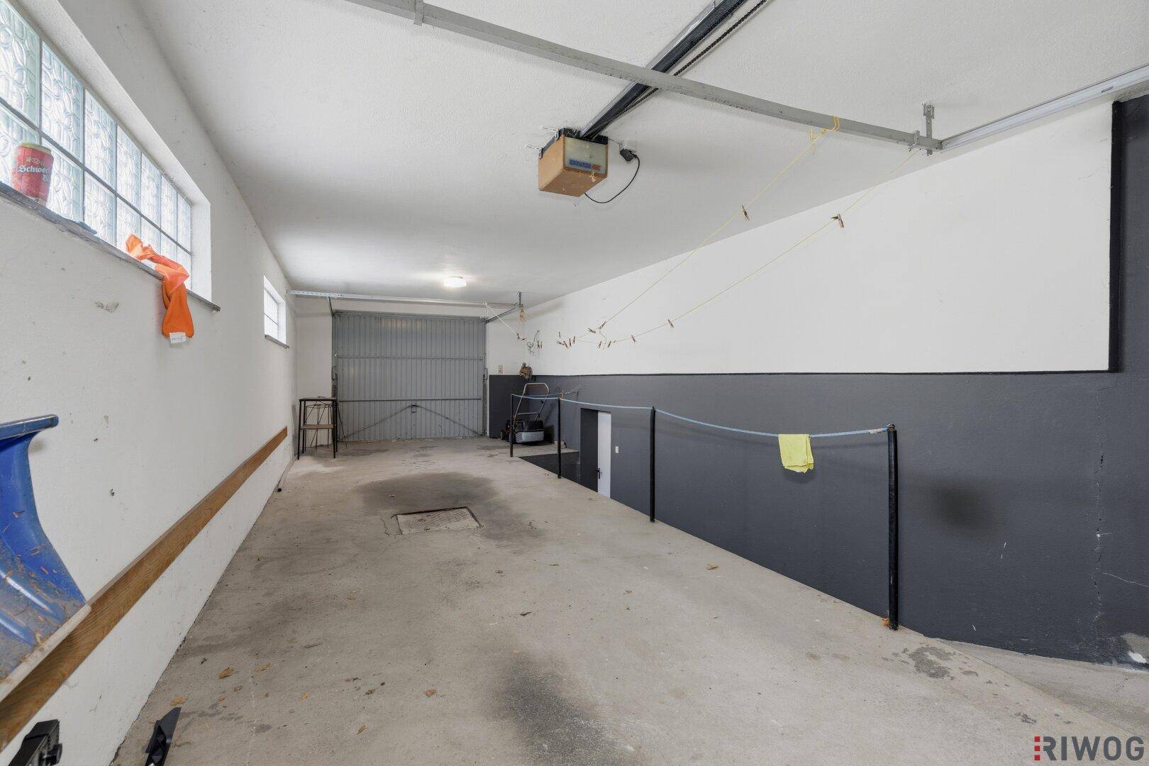 Geräumige Garage mit Betonboden, Schwingtor und kleinen Fenstern für Belüftung.