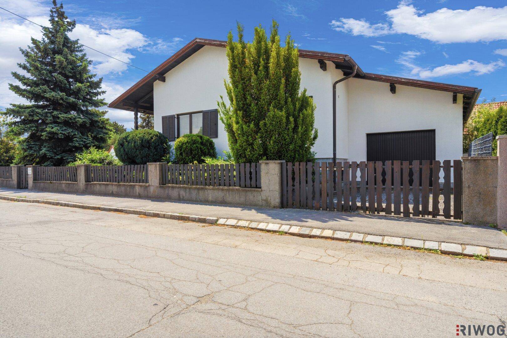 Ansicht des Einfamilienhauses von der Straße mit dunklem Holzzaun und gepflegter Bepflanzung.