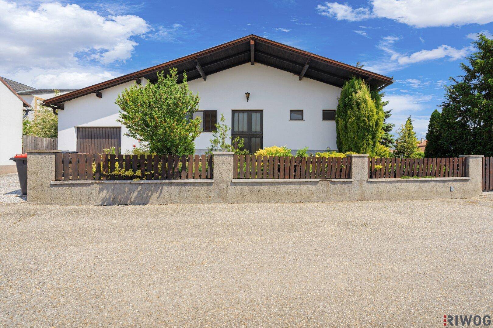 Einfamilienhaus mit weißer Fassade, Holzzaun und Satteldach von der Straße aus gesehen.