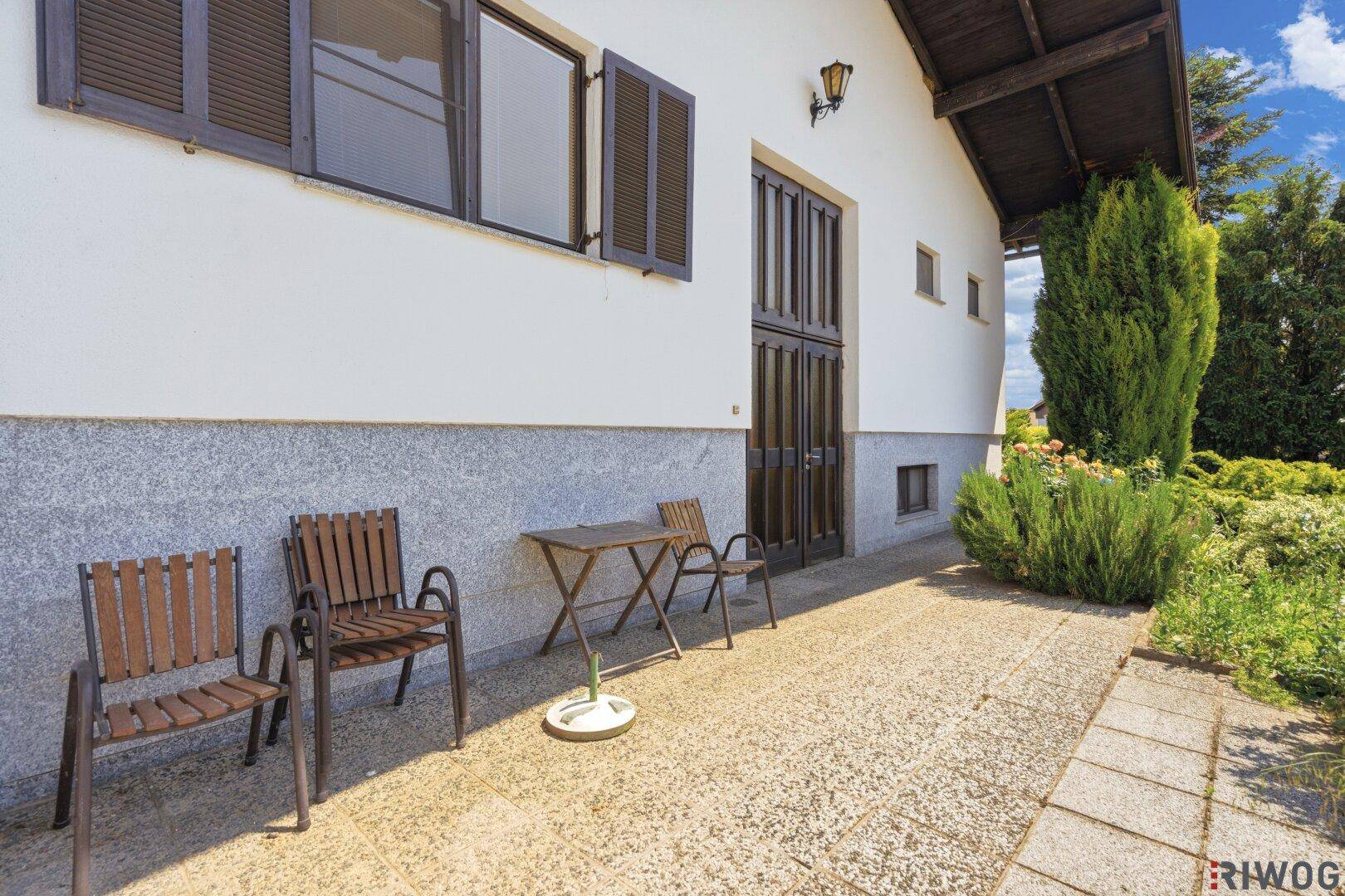 Kleine Terrasse mit einfachen Gartenmöbeln neben dem Haus und Zugang zum Garten.
