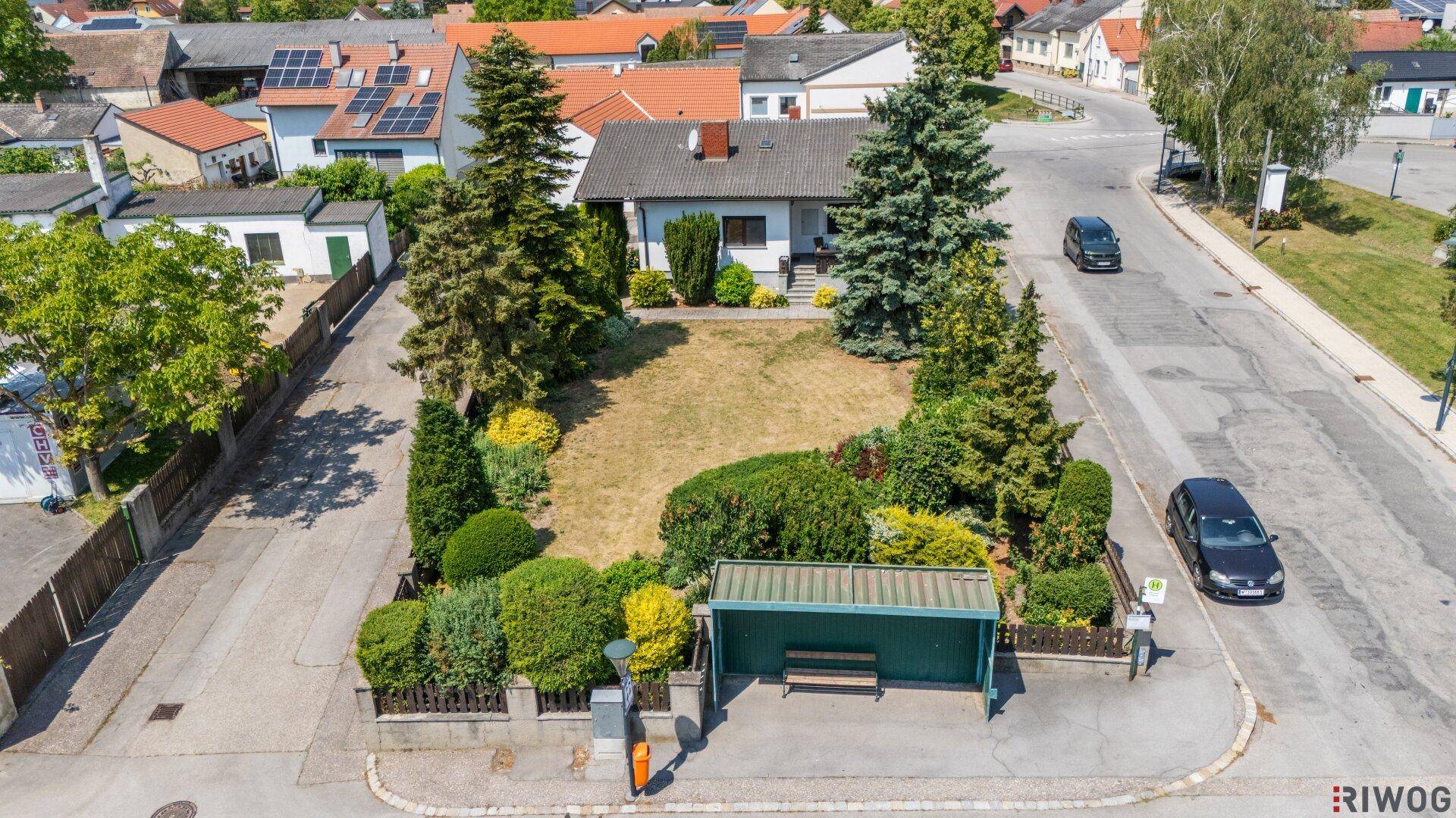 Luftaufnahme eines Einfamilienhauses mit Garten und Bushaltestelle in einer Wohnsiedlung.