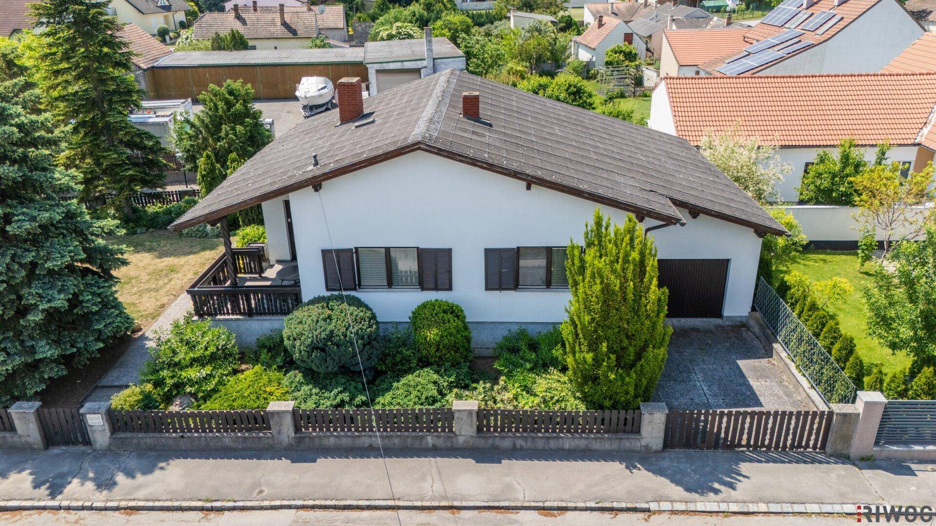 Luftaufnahme der Vorderseite eines Einfamilienhauses mit Garage und gepflegtem Vorgarten.