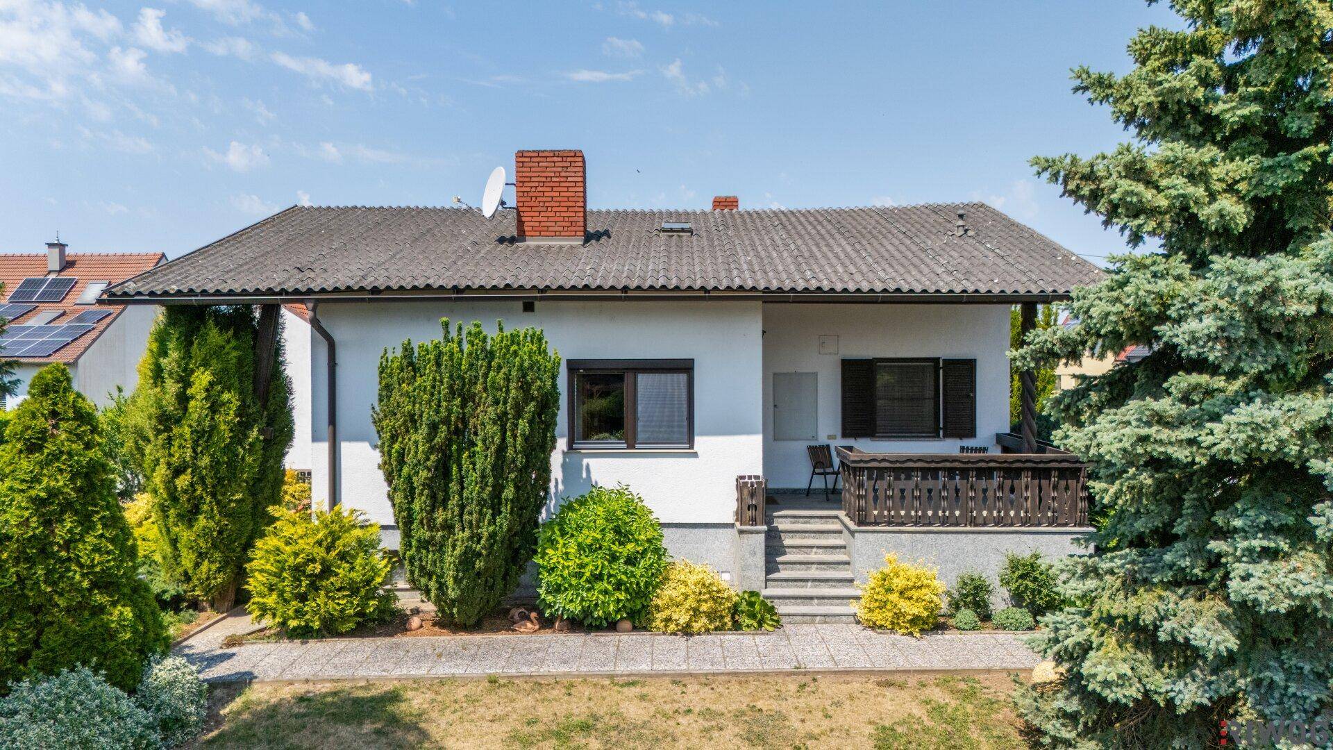 Vorderansicht eines Einfamilienhauses mit weißer Fassade, Satteldach und grüner Bepflanzung.