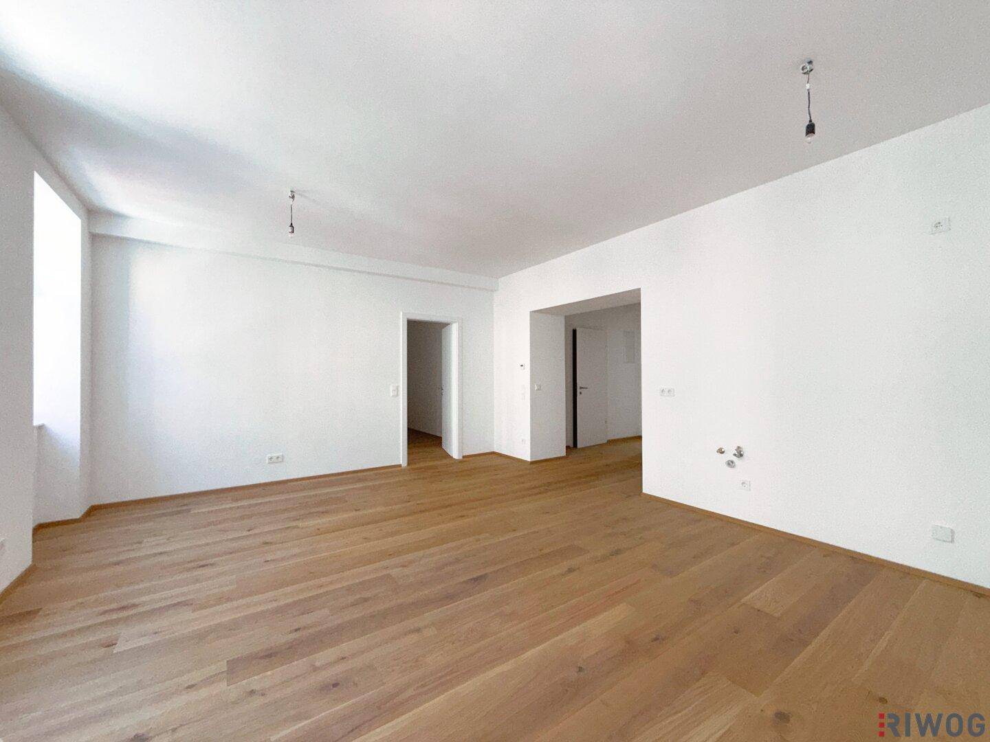 Großer, heller Wohnbereich mit Holzboden und Zugang zu weiteren Räumen der Wohnung.