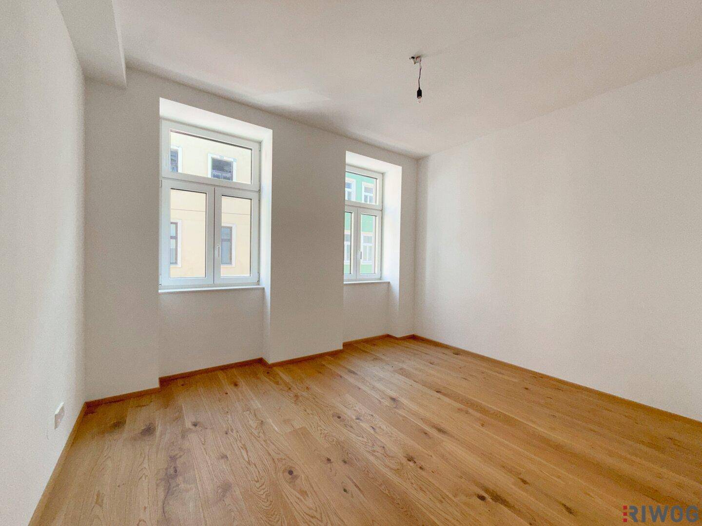 Helles Schlafzimmer mit Holzboden und zwei Fenstern, bietet viel Tageslicht und Stadtblick.