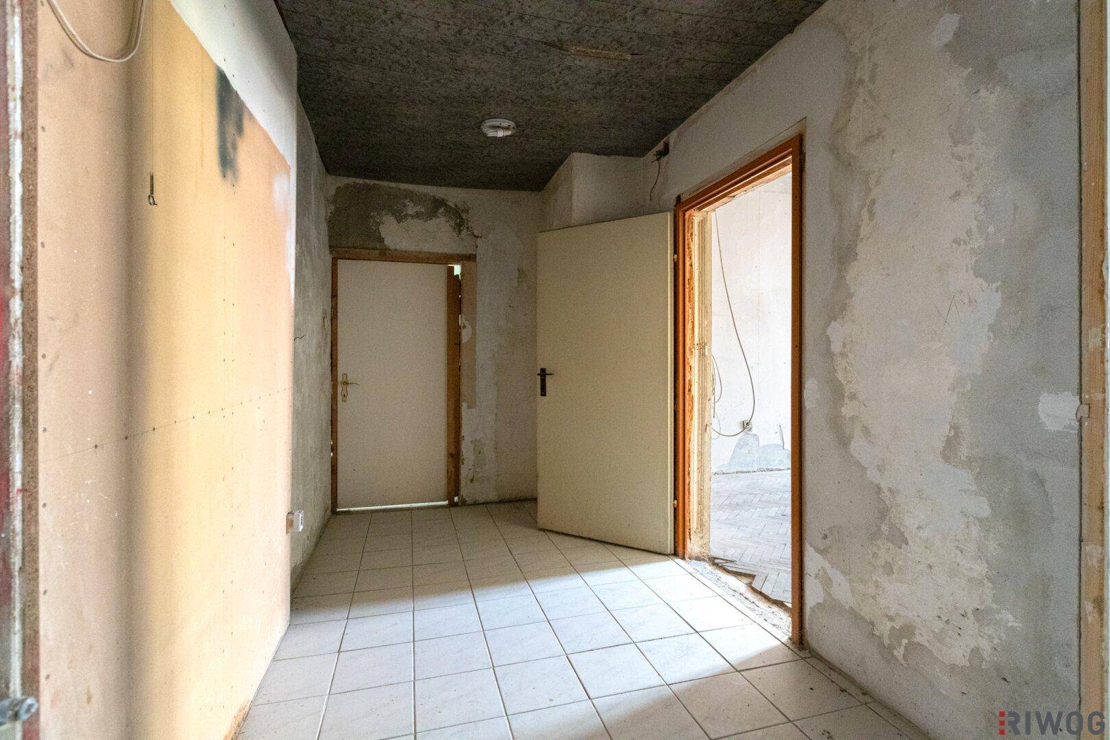 Flur mit Fliesenboden und unfertigen Wänden, der auf eine Renovierung wartet.