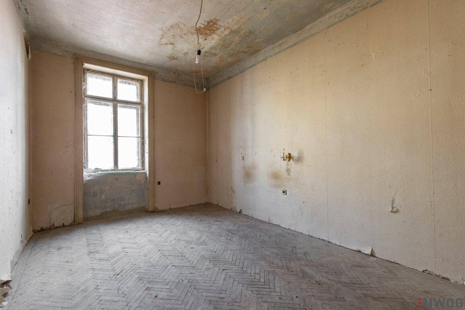 Unrenoviertes Schlafzimmer mit abgenutztem Fischgrätparkett und Fenster, bereit zur Sanierung.