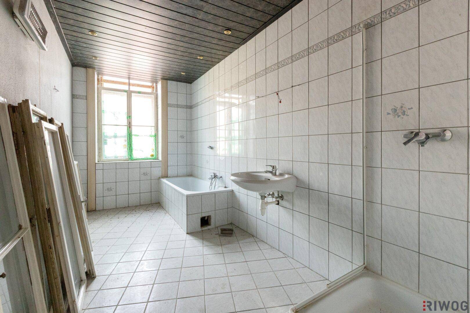 Badezimmer mit Badewanne, Waschbecken und Fliesen, das eine umfassende Renovierung benötigt.