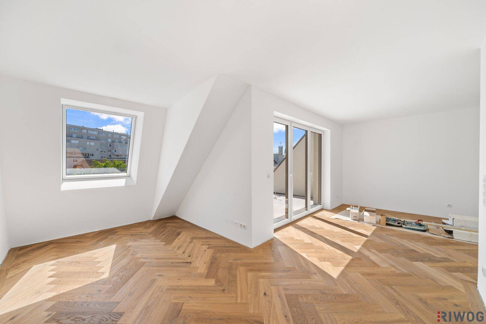 Helles Schlafzimmer mit Fischgrätparkett, Dachschräge und Zugang zu einem Balkon.