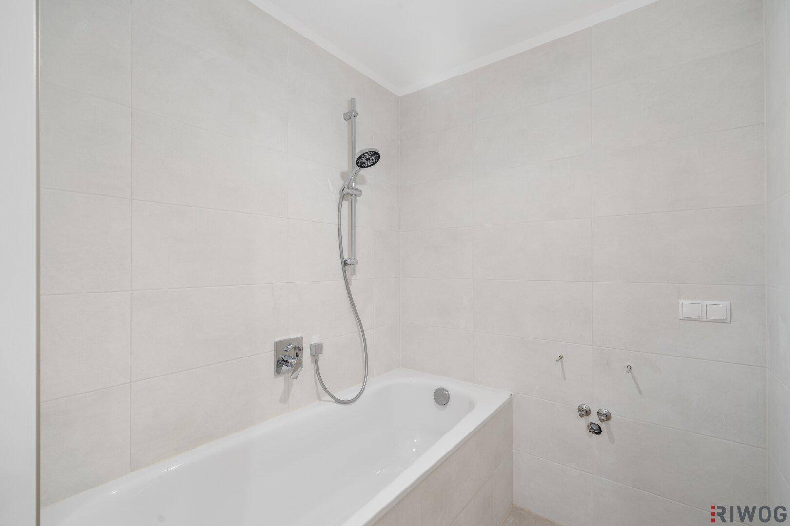 Modern gefliestes Badezimmer mit Badewanne und Duscharmatur, bereit zur Fertigstellung.