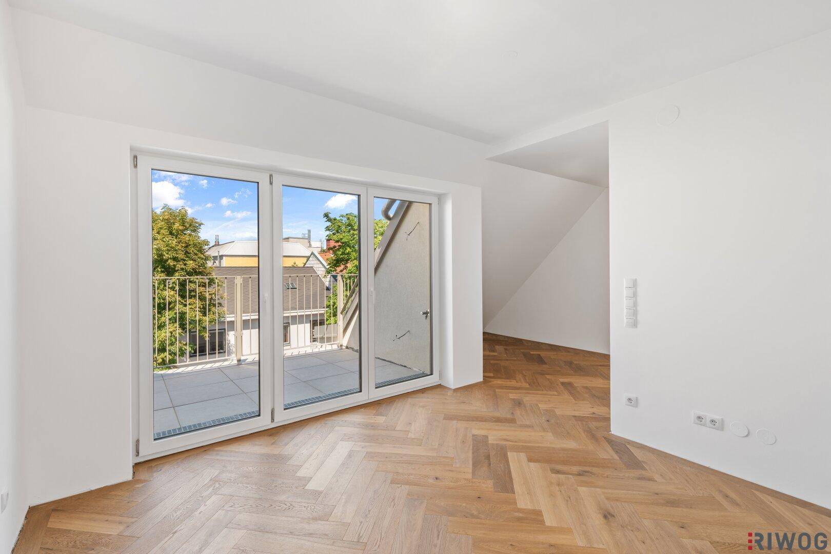 Heller Wohnbereich mit Fischgrätparkett und Zugang zu einem sonnigen Balkon.