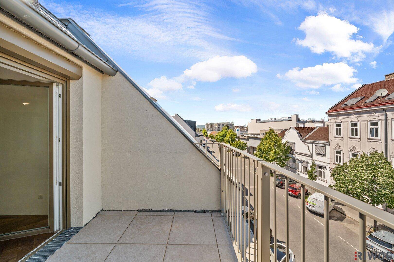 Geräumiger Balkon mit Fliesenboden und Blick auf die Straße und umliegende Gebäude.