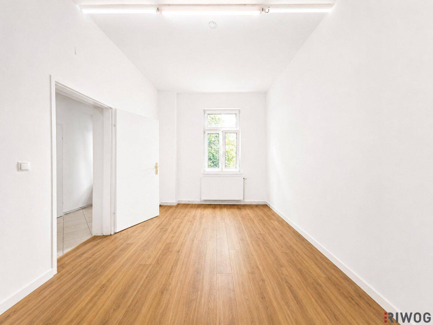 Ruhiges Zimmer mit Laminatboden, weiß gestrichenen Wänden und einem Fenster, das eine angenehme Atmosphäre schafft.