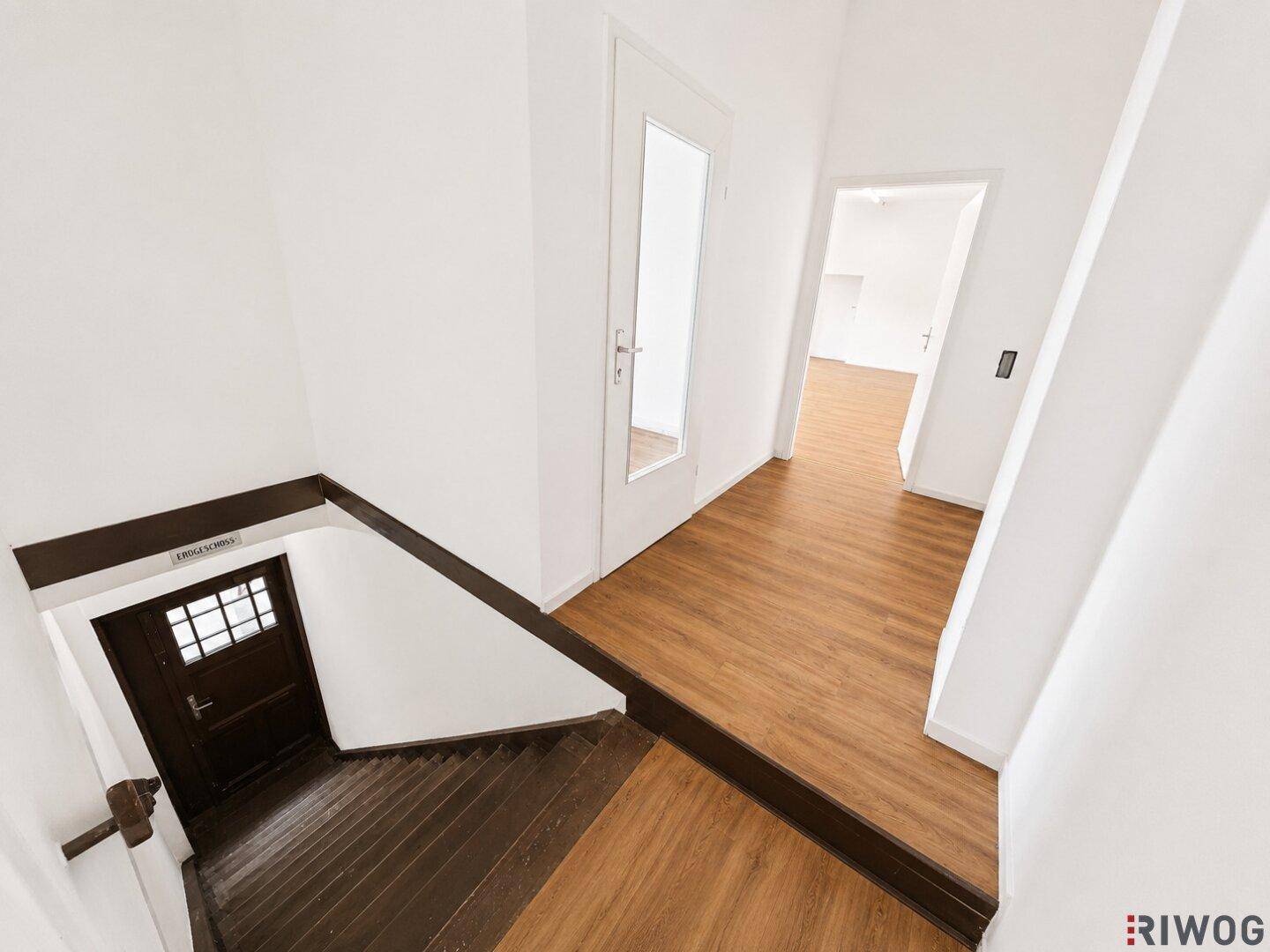 Treppenabsatz mit Laminatboden und einer Tür, die zu weiteren Räumen führt, mit Blick auf die Holztreppe.