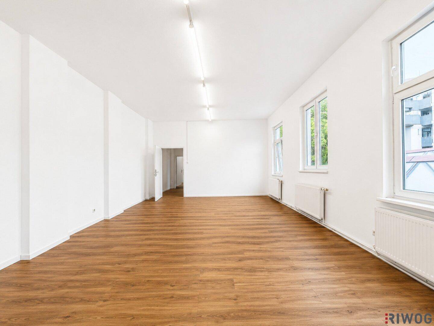 Heller Wohnraum mit Laminatboden und mehreren Fenstern, die viel Tageslicht hereinlassen, in einem gepflegten Zustand.