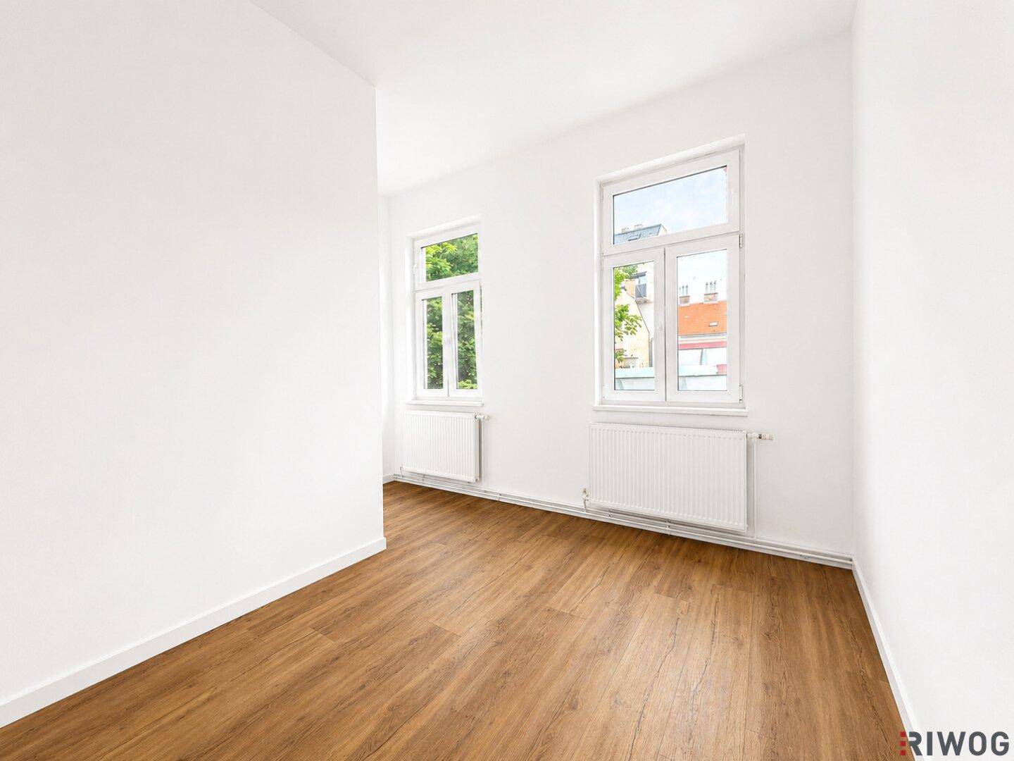 Helles Zimmer mit zwei Fenstern, Laminatboden und weißen Wänden, das viel Potenzial für individuelle Gestaltung bietet.