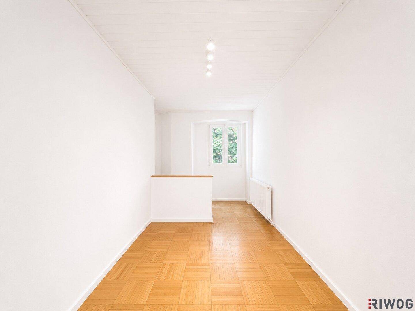 Gemütliches Zimmer mit Parkettboden, weißen Wänden und einem Fenster, das eine helle und einladende Atmosphäre schafft.