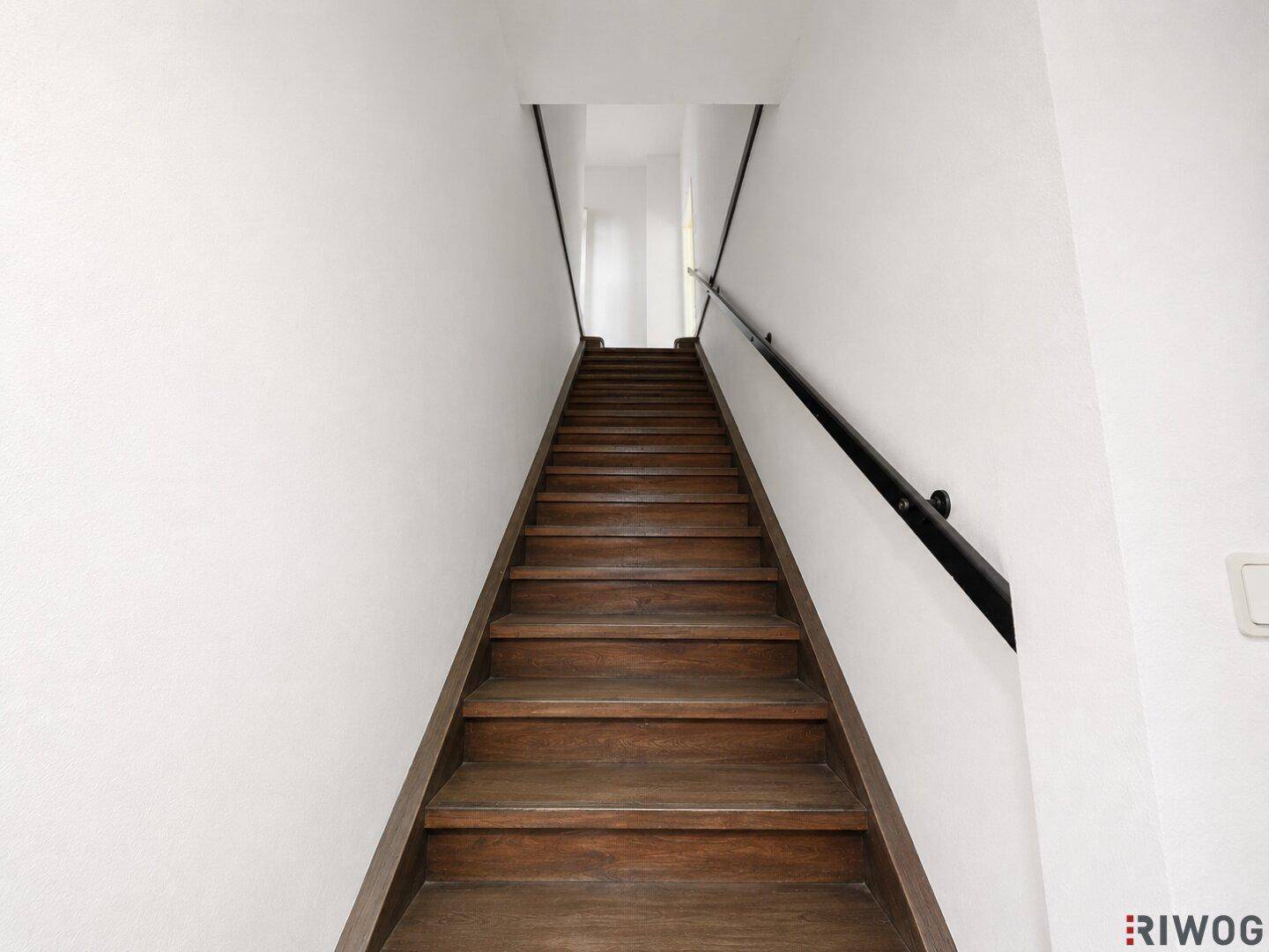 Elegante Holztreppe mit schwarzem Handlauf und weißen Wänden, die zu den oberen Etagen führt.