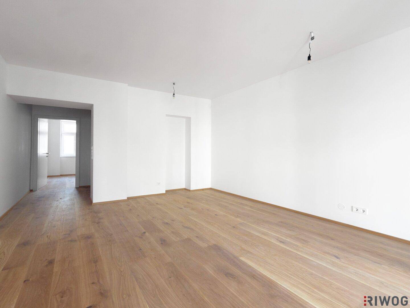 Weitläufiges Wohnzimmer mit neuem Parkettboden und Zugang zu weiteren Räumen.