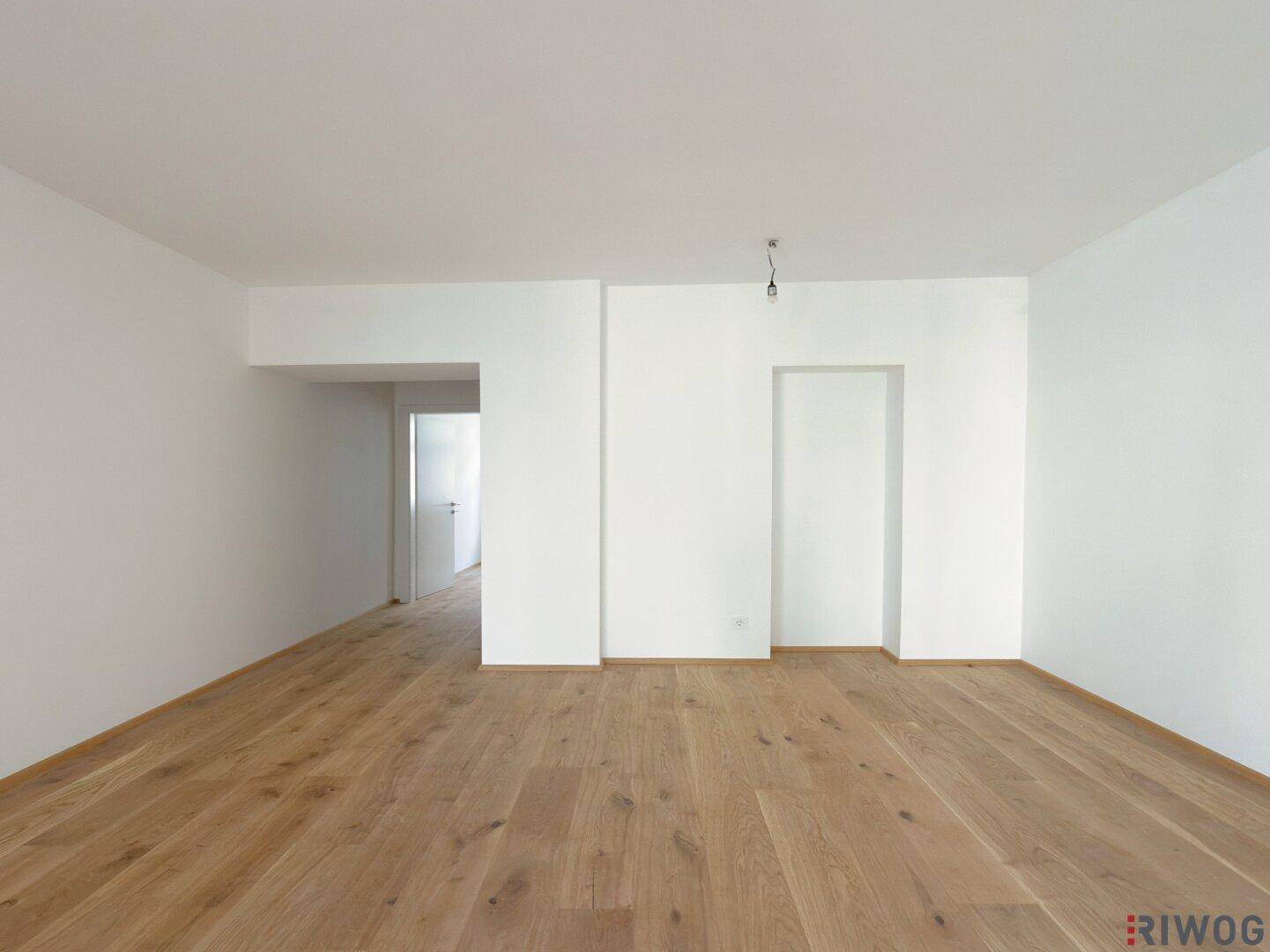 Unmöbliertes Wohnzimmer mit weiß gestrichenen Wänden und hochwertigem Parkettboden.